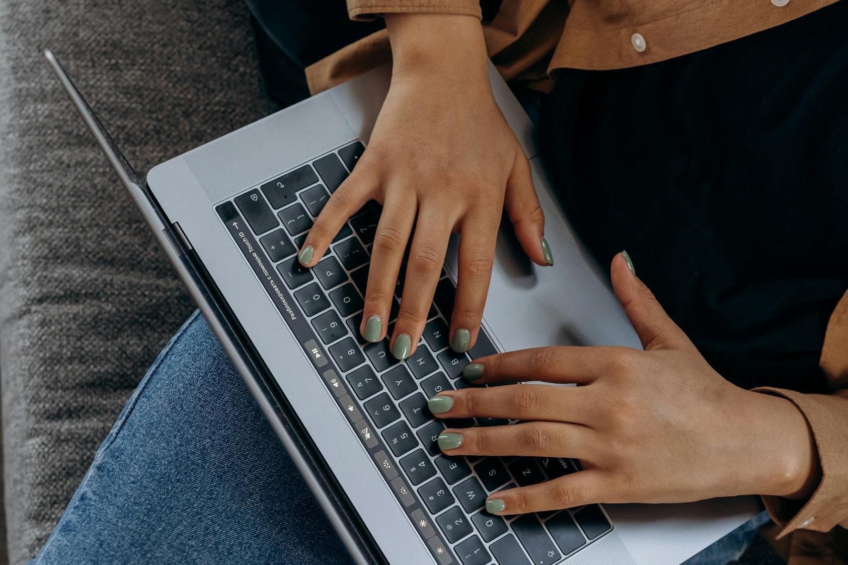 A person typing on a laptop while seated on a couch with casual attire, perfect for remote work imagery.